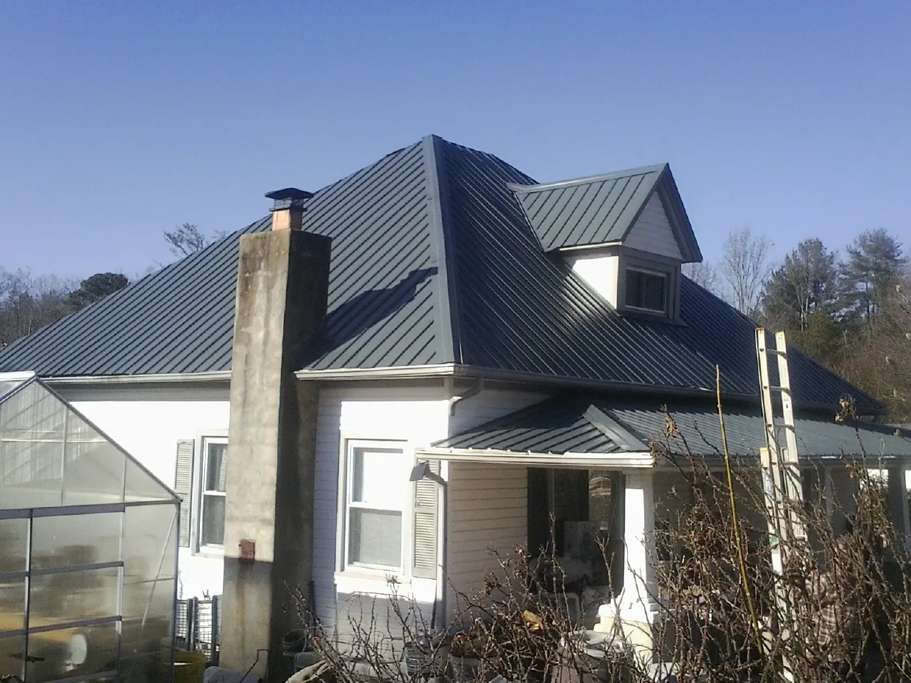 Dark blue standing seam metal roof on a white farmhouse with dormer — Slate & Tile Roof Repair by Roofing Brothers in Henryetta