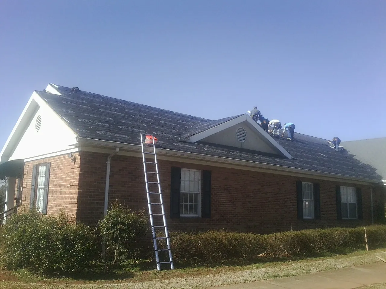 Crew tearing shingles off a brick ranch roof with a ladder set — Metal Roof Repair work by our crew in Henryetta