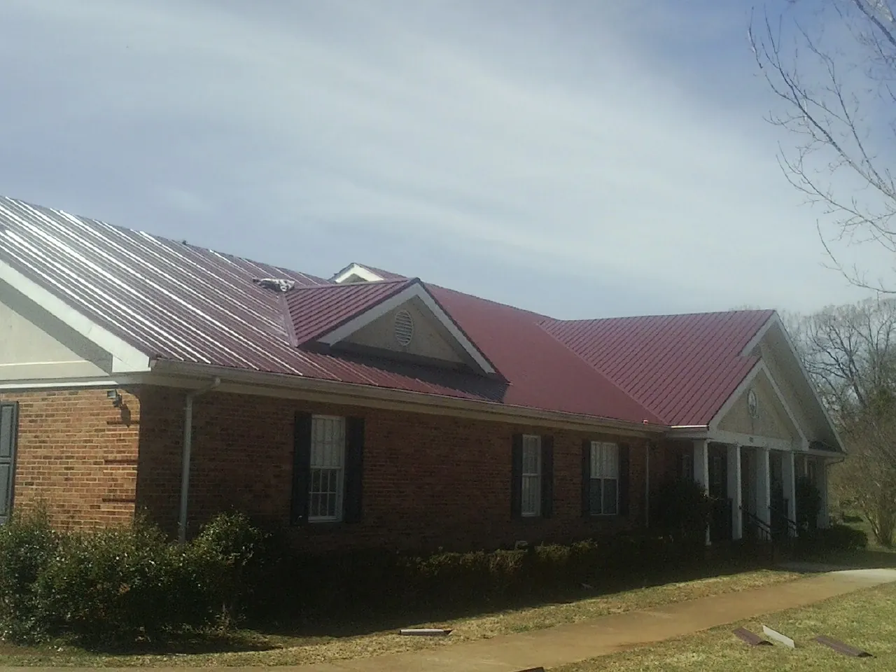 Red metal roof with gabled entries on a long brick building, from a Hail Damage Roof Repair job in Henryetta