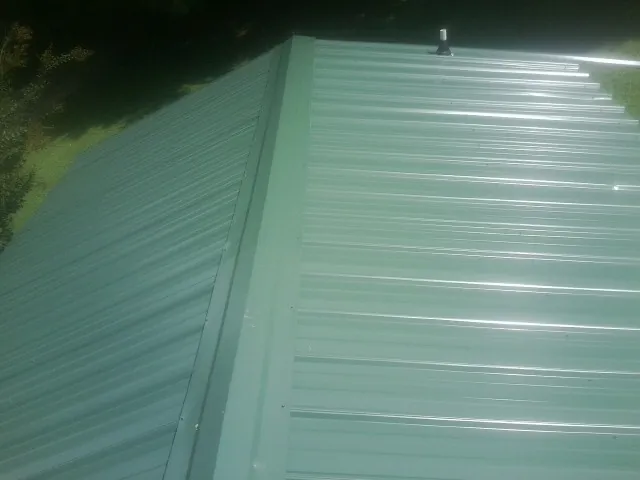 New green metal panels meeting at the ridge of a roof — Flat Roof Repair work by our crew in Henryetta