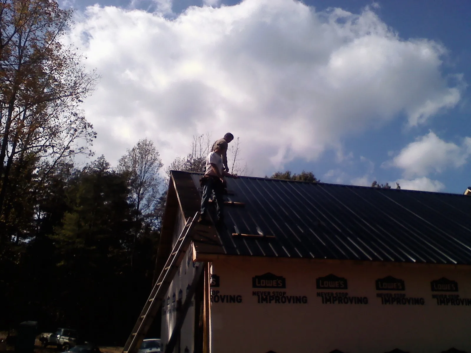 Roofer fastening dark metal panels high against a cloudy sky, from a Roof Inspection job in Henryetta