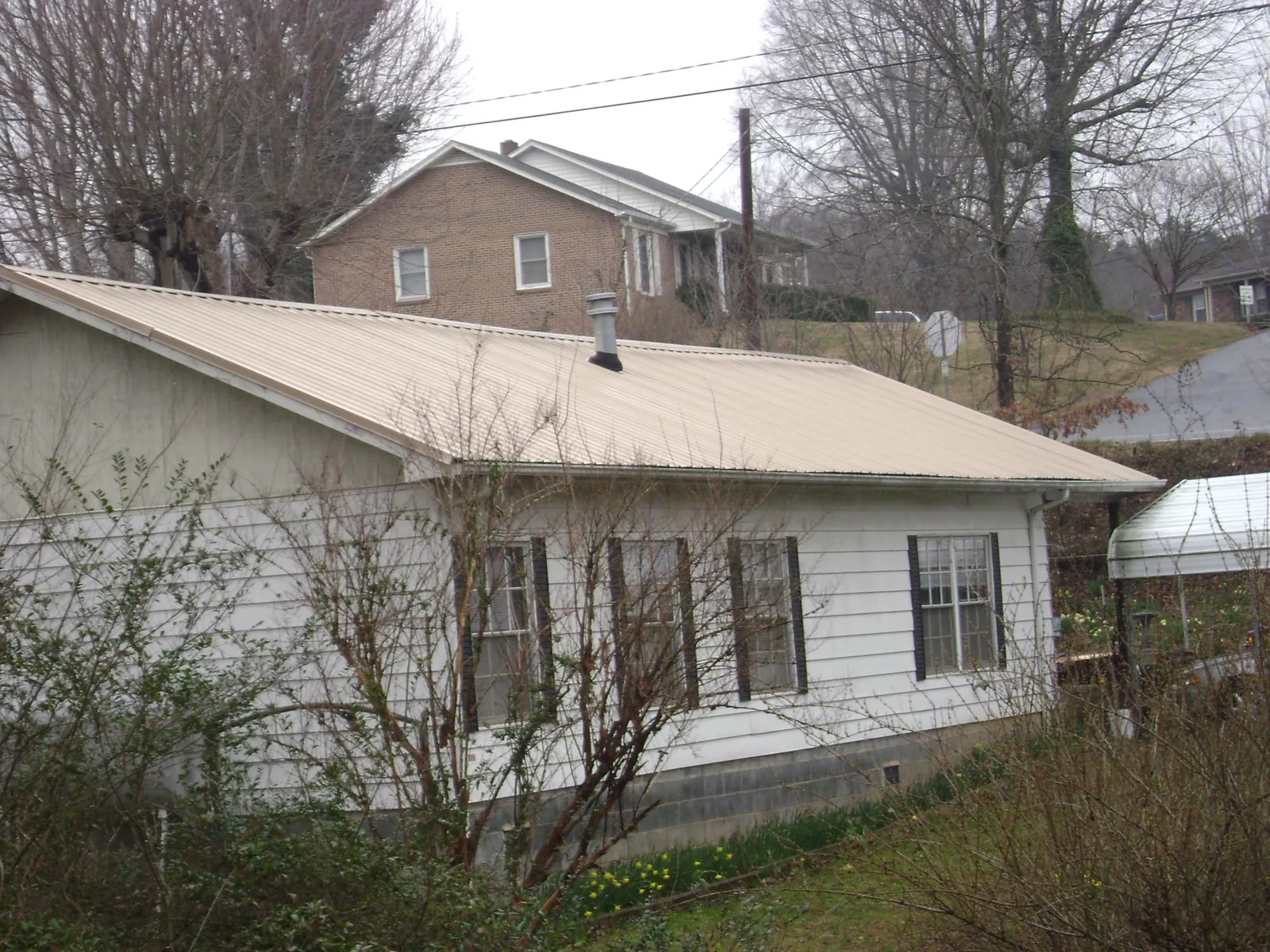 Tan metal roof on a white sided house set into a hillside — Commercial Roofing by Roofing Brothers in Henryetta