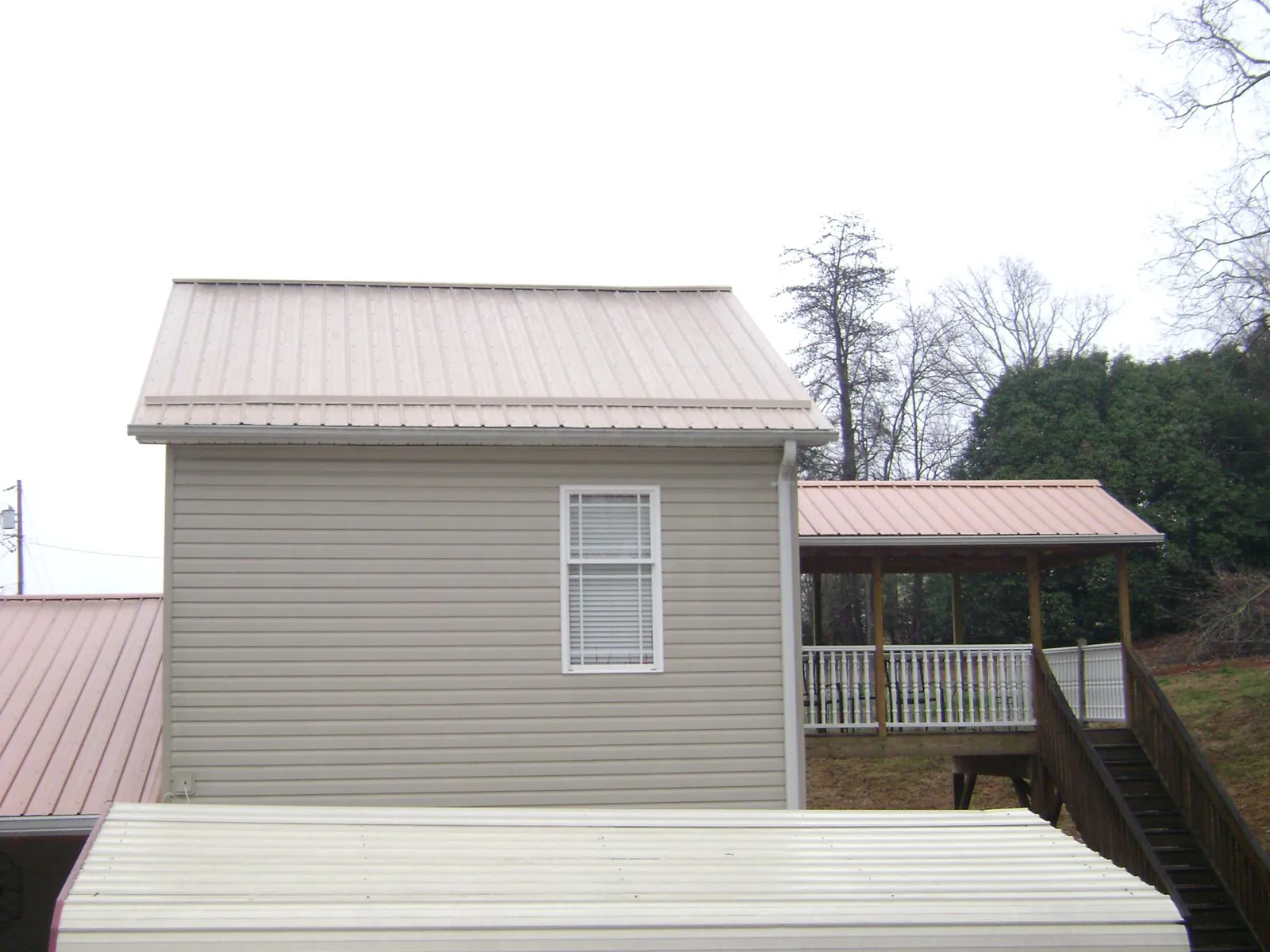 Tan metal roofs on a two story addition and attached porch, from a Roof Replacement job in Henryetta